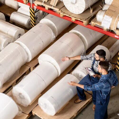 Workers examine huge rolls of paper at a paper warehouse